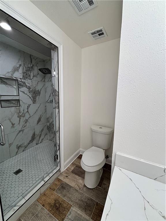 bathroom with toilet, a marble finish shower, and visible vents