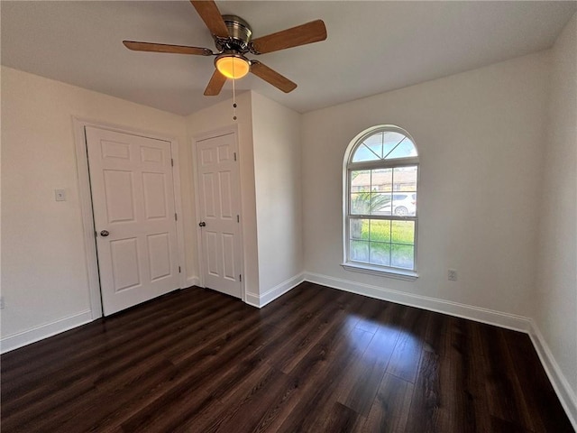 spare room featuring dark wood finished floors, a ceiling fan, and baseboards