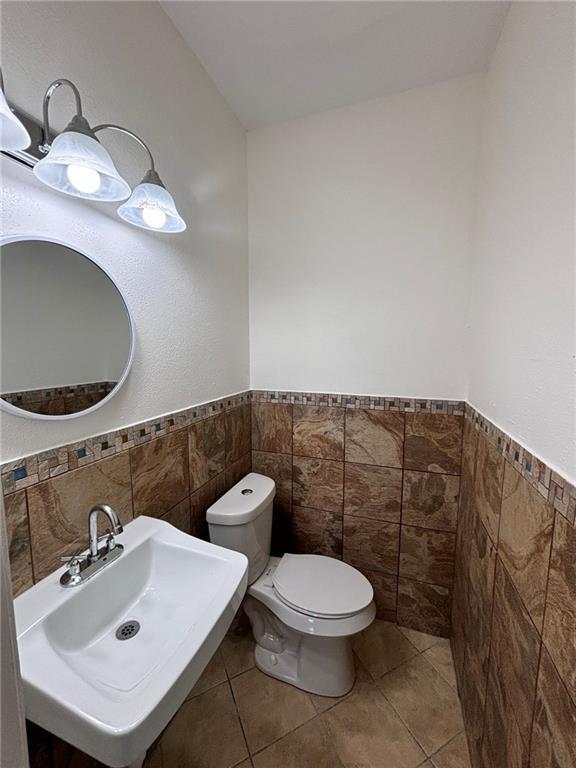 half bathroom with a wainscoted wall, a sink, toilet, and tile patterned floors