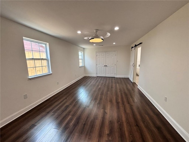 empty room featuring a barn door, dark wood-style flooring, recessed lighting, and baseboards