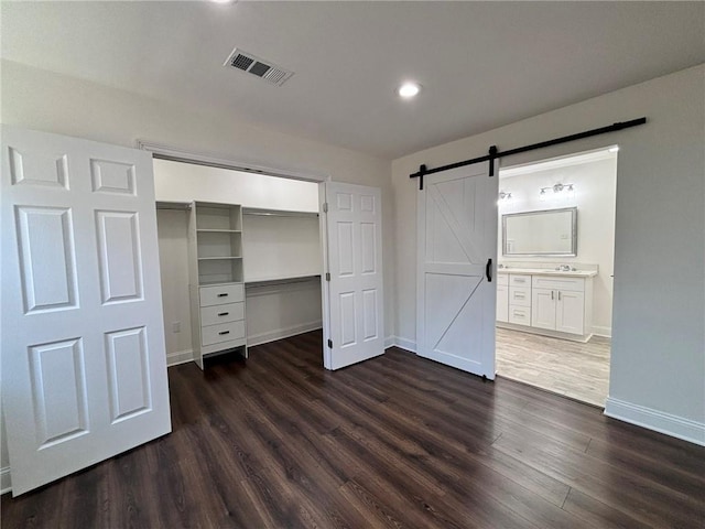 unfurnished bedroom featuring a barn door, visible vents, baseboards, a closet, and dark wood-style floors