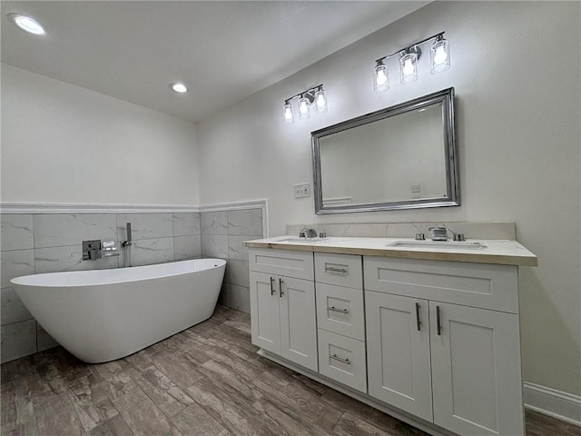 full bath with double vanity, wood finished floors, a freestanding tub, and a sink