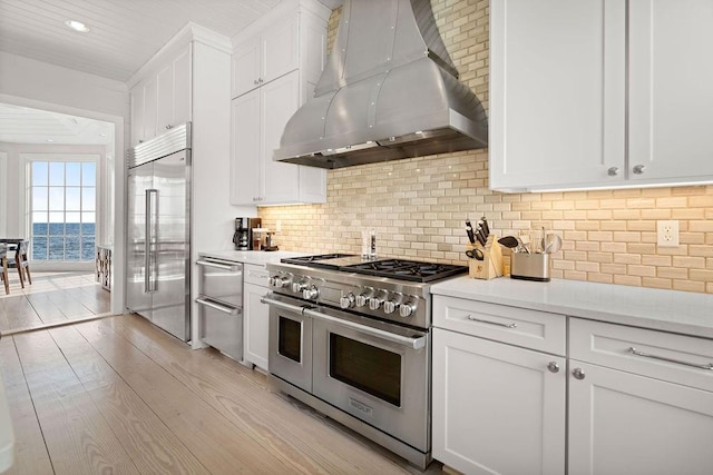 kitchen featuring backsplash, light hardwood / wood-style flooring, white cabinetry, wall chimney exhaust hood, and high quality appliances