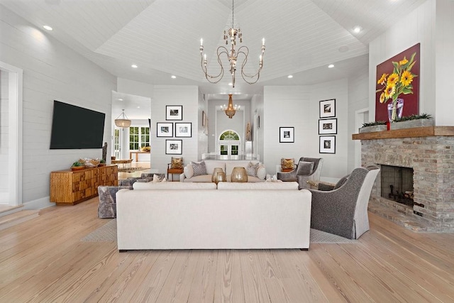 living room featuring light wood-type flooring, an inviting chandelier, and a stone fireplace