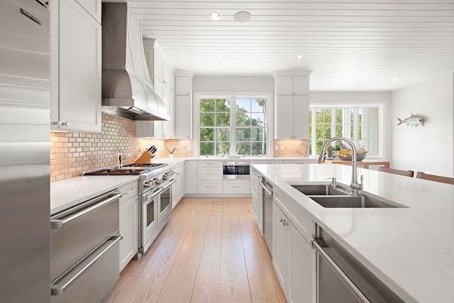 kitchen featuring sink, custom range hood, appliances with stainless steel finishes, light hardwood / wood-style floors, and white cabinetry