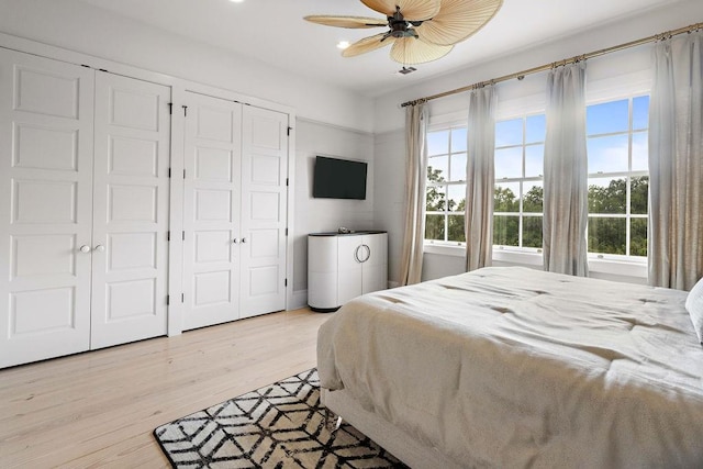 bedroom featuring ceiling fan, multiple closets, and light hardwood / wood-style flooring