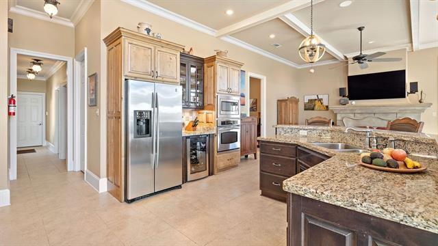 kitchen with light stone counters, beverage cooler, ceiling fan, ornamental molding, and appliances with stainless steel finishes