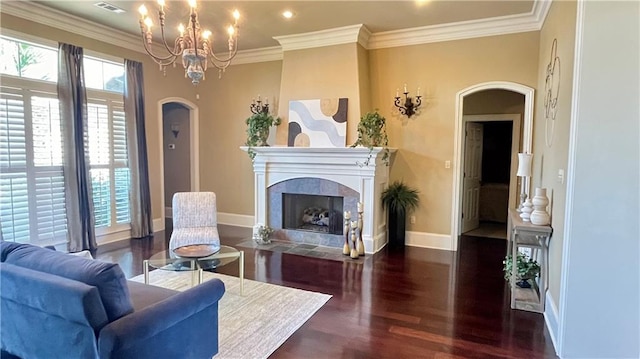 living room with a tiled fireplace, dark wood-type flooring, ornamental molding, and an inviting chandelier