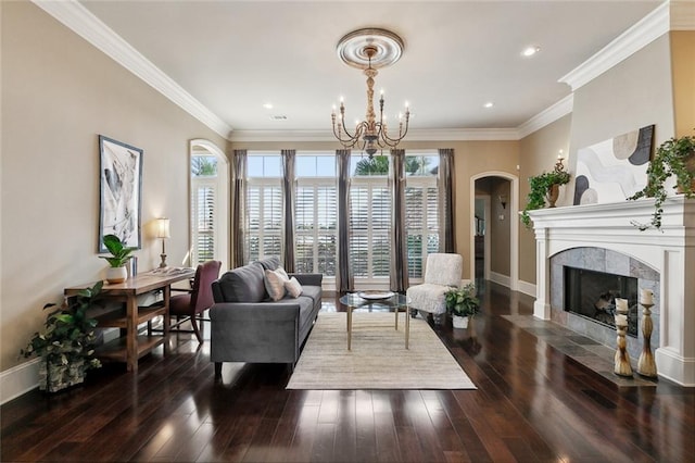 living room featuring crown molding, baseboards, a premium fireplace, hardwood / wood-style floors, and an inviting chandelier