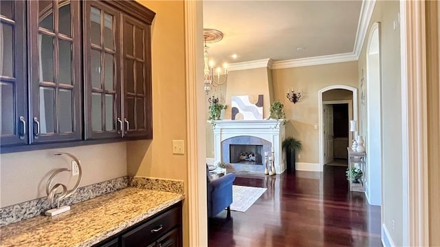 interior space with dark wood-type flooring, arched walkways, a fireplace, crown molding, and baseboards