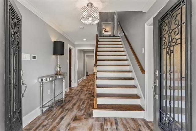 entryway featuring baseboards, ornamental molding, dark wood-type flooring, an inviting chandelier, and stairs