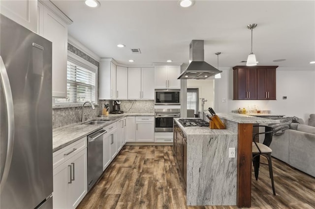 kitchen with island range hood, white cabinets, appliances with stainless steel finishes, decorative light fixtures, and a sink