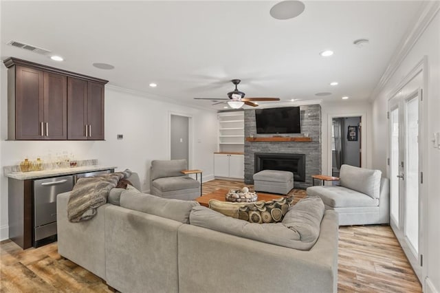 living area with a dry bar, visible vents, ornamental molding, light wood-type flooring, and a fireplace