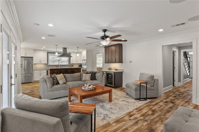 living area with light wood finished floors, visible vents, wine cooler, crown molding, and recessed lighting