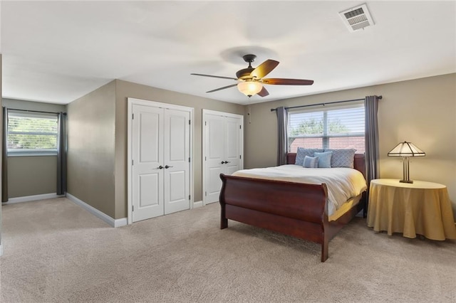 bedroom featuring multiple closets, light colored carpet, visible vents, a ceiling fan, and baseboards