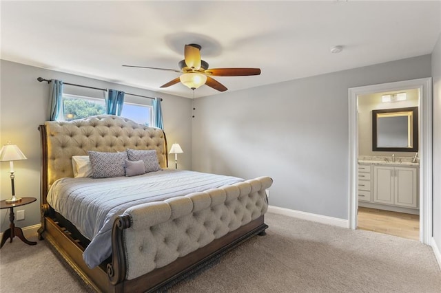 bedroom with baseboards, ensuite bathroom, a ceiling fan, and light colored carpet