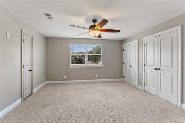 unfurnished bedroom with baseboards, visible vents, two closets, and light colored carpet