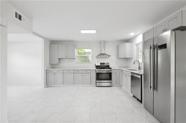 kitchen with light tile patterned flooring, sink, appliances with stainless steel finishes, gray cabinets, and wall chimney range hood