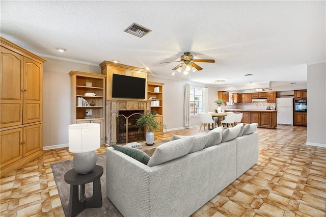 living room with ceiling fan, light tile patterned floors, ornamental molding, and a textured ceiling