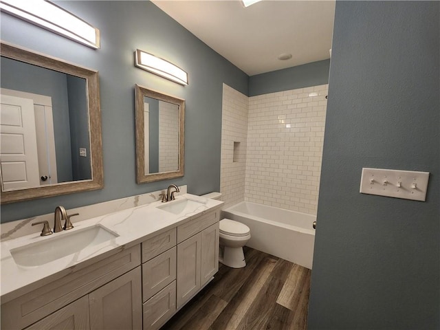 full bathroom featuring tiled shower / bath combo, hardwood / wood-style floors, dual vanity, and toilet