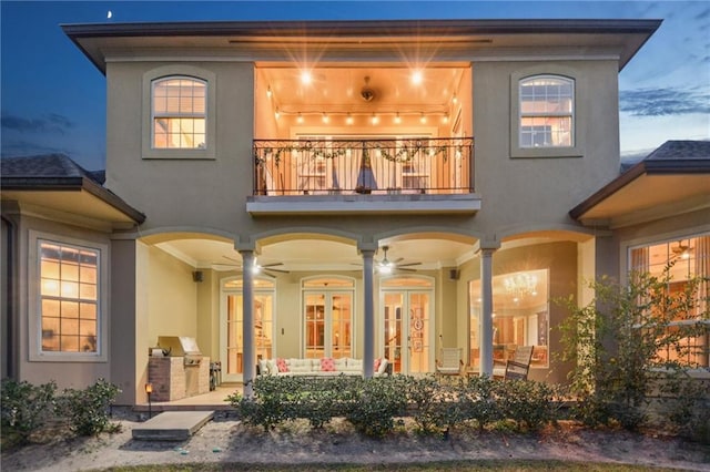 back house at dusk with a balcony, ceiling fan, and exterior kitchen