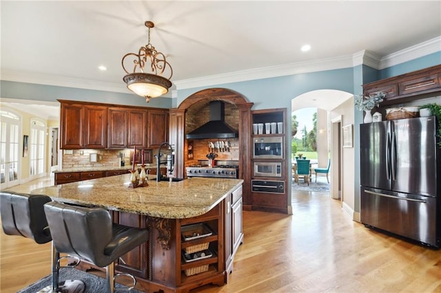 kitchen with an island with sink, light wood-type flooring, decorative backsplash, appliances with stainless steel finishes, and custom exhaust hood