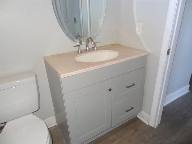 half bathroom featuring baseboards, vanity, toilet, and wood finished floors