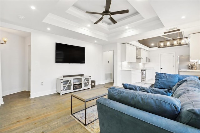 living room featuring ceiling fan, light hardwood / wood-style floors, and a raised ceiling