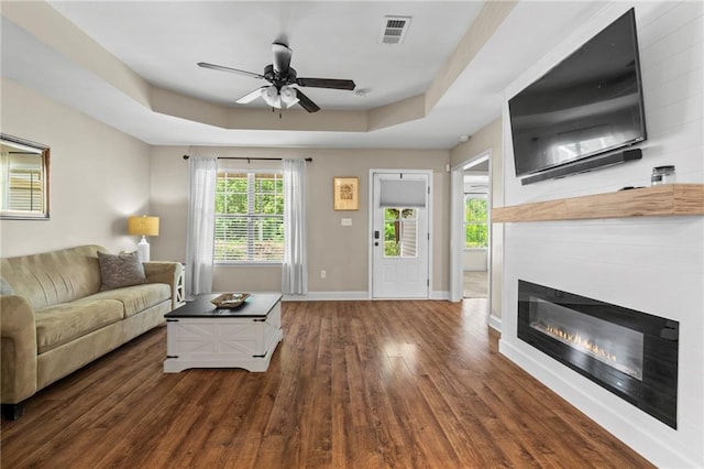 living room with ceiling fan, a raised ceiling, and dark hardwood / wood-style floors