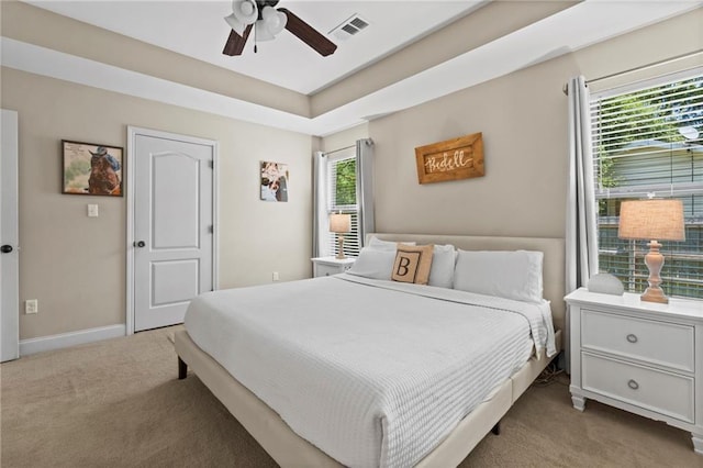 carpeted bedroom featuring a tray ceiling, baseboards, visible vents, and ceiling fan
