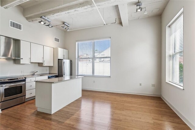 kitchen with light wood finished floors, wall chimney exhaust hood, visible vents, and appliances with stainless steel finishes