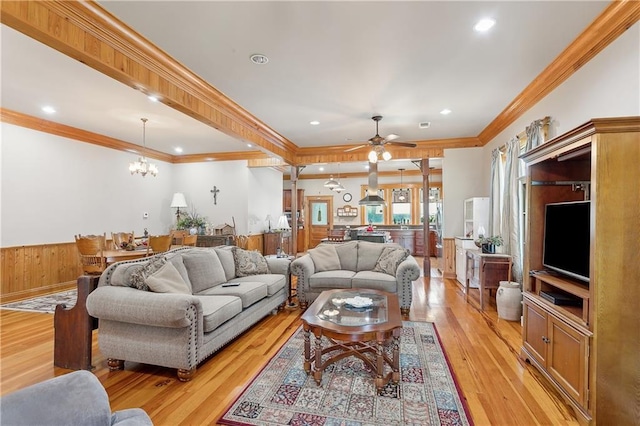 living room with ceiling fan with notable chandelier, light wood-type flooring, crown molding, and wooden walls