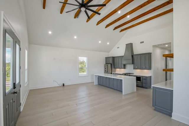 kitchen with beamed ceiling, custom range hood, an island with sink, and ceiling fan