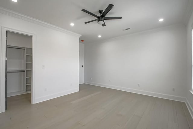 unfurnished bedroom with ceiling fan, a spacious closet, a closet, hardwood / wood-style flooring, and crown molding