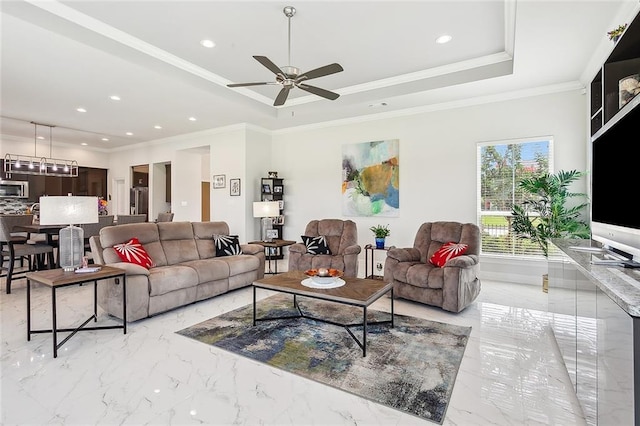 living room with ceiling fan with notable chandelier, ornamental molding, and a tray ceiling