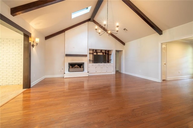 unfurnished living room with wood-type flooring, beam ceiling, high vaulted ceiling, a large fireplace, and a skylight