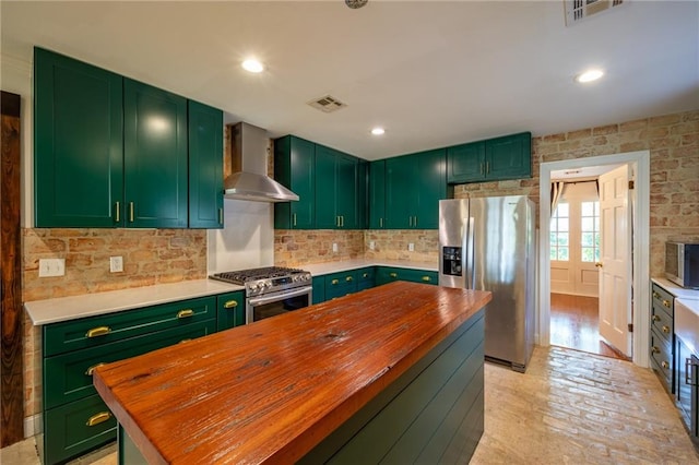 kitchen featuring green cabinetry, appliances with stainless steel finishes, wall chimney exhaust hood, and butcher block counters