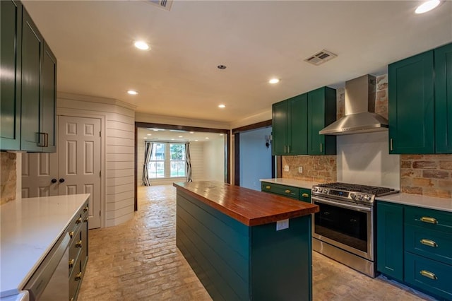 kitchen with tasteful backsplash, stainless steel gas stove, butcher block counters, a kitchen island, and wall chimney range hood