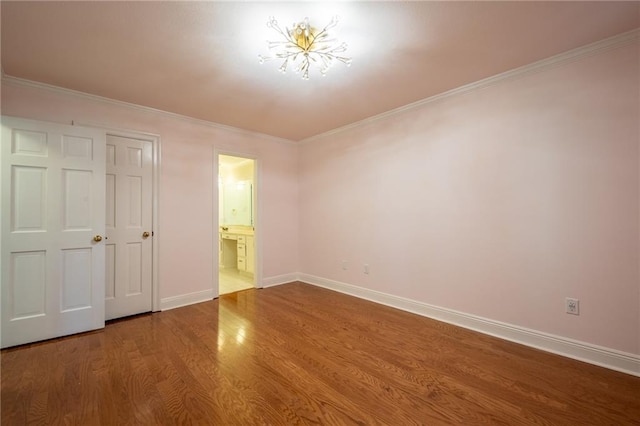 unfurnished bedroom with connected bathroom, an inviting chandelier, wood-type flooring, and crown molding