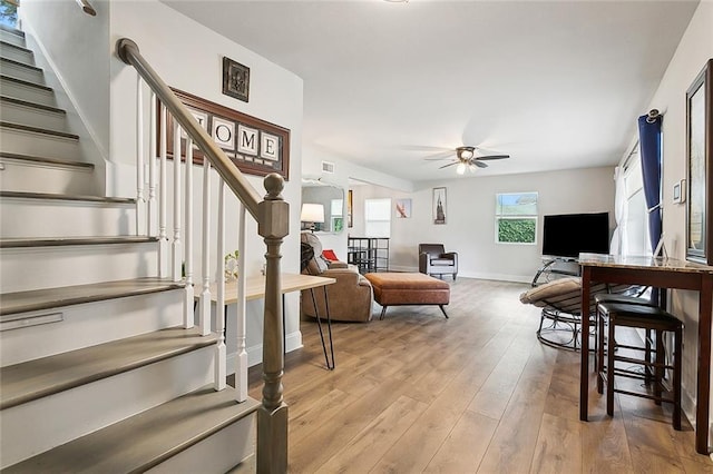 living room with baseboards, light wood-style flooring, stairway, and a ceiling fan