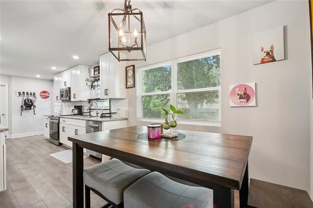 dining space featuring sink, light wood-type flooring, and a notable chandelier