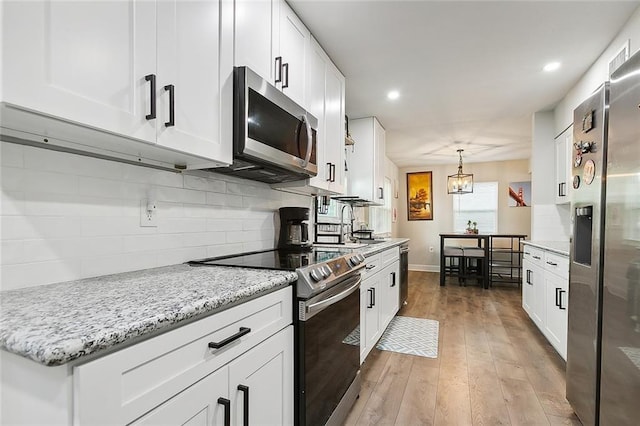 kitchen featuring stainless steel appliances, decorative backsplash, light wood-type flooring, pendant lighting, and white cabinets