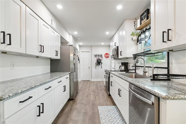 kitchen with backsplash, light wood-type flooring, appliances with stainless steel finishes, light stone countertops, and white cabinets