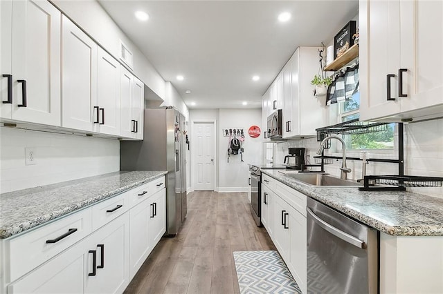 kitchen featuring open shelves, stainless steel appliances, white cabinetry, a sink, and light stone countertops