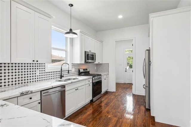 kitchen featuring appliances with stainless steel finishes, dark hardwood / wood-style floors, sink, light stone counters, and hanging light fixtures