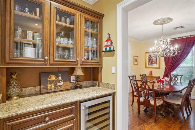 bar with a chandelier, dark hardwood / wood-style floors, light stone counters, pendant lighting, and beverage cooler