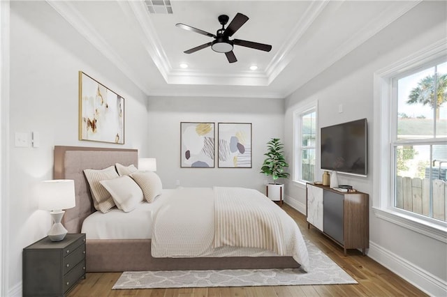 bedroom with a raised ceiling, visible vents, ornamental molding, wood finished floors, and baseboards