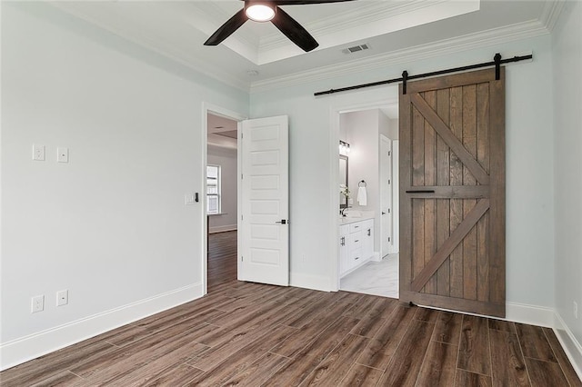 unfurnished bedroom with ceiling fan, ensuite bathroom, a barn door, and wood-type flooring