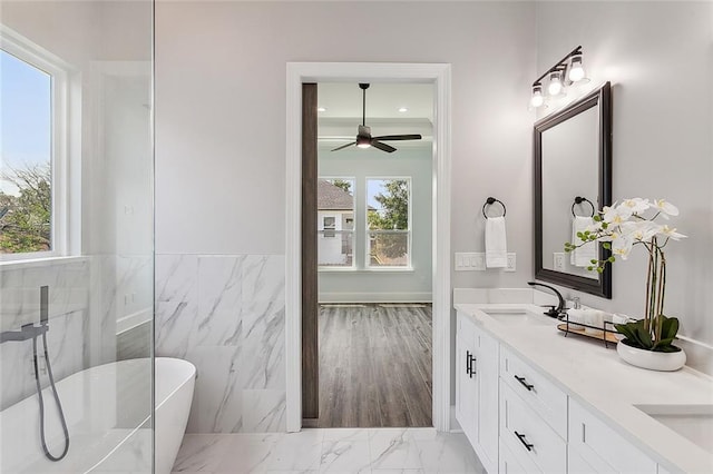 bathroom featuring a washtub, hardwood / wood-style floors, vanity, tile walls, and ceiling fan