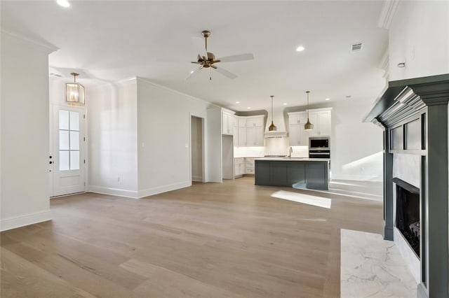 unfurnished living room featuring light wood-type flooring, ceiling fan, crown molding, a premium fireplace, and sink